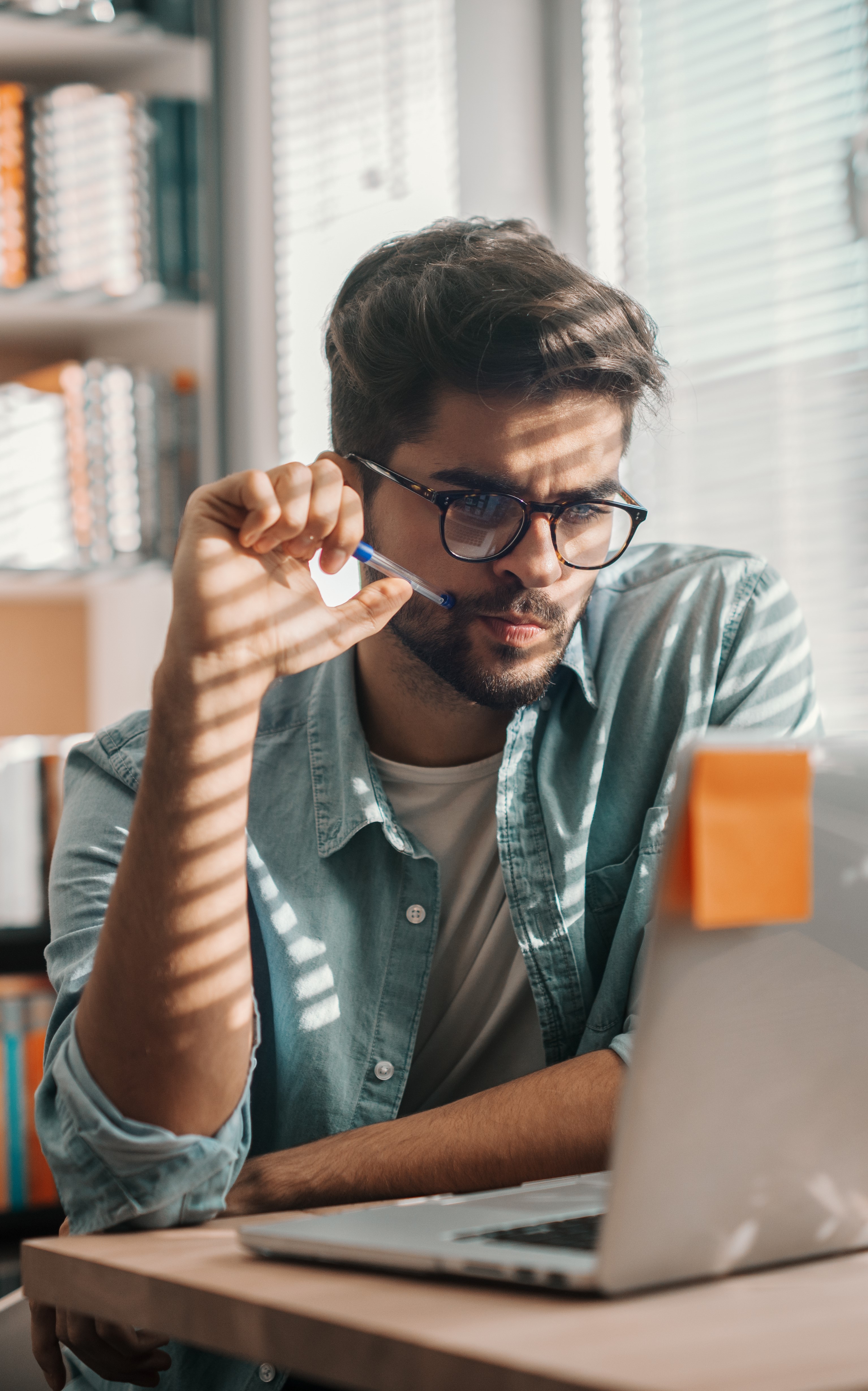 Male student looking at laptop with pen in hand