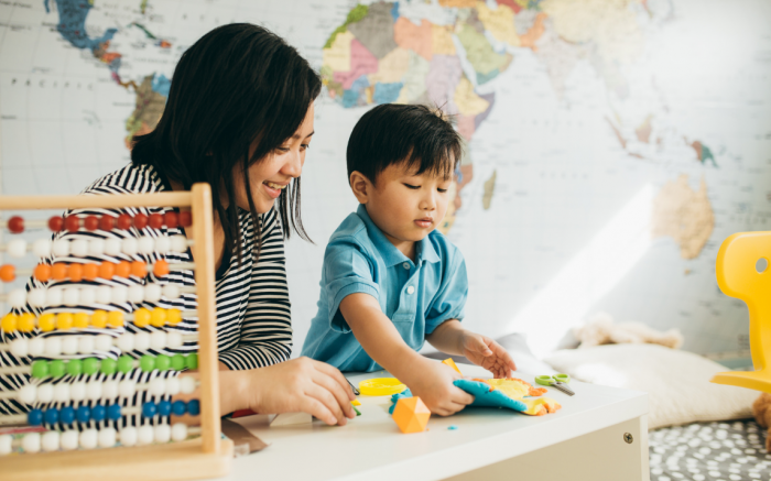 Female smiling at toddler who is playing with clay