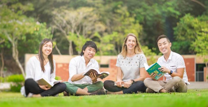 Students sitting on grass smiling into camera