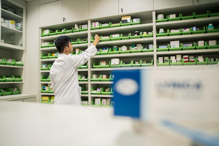 Student wearing medical gown browsing at medicines on shelf