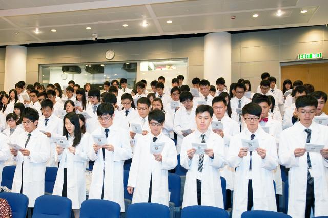 Students wearing medical gown looking at card in hand in a lecture hall