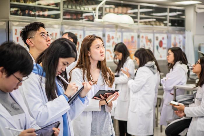 Students wearing white gown with tablets in hand looking focused