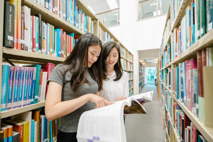 Students pointing at an open book in library