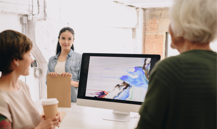 Group of modern creative people looking at a computer screen with abstract painting in design studio